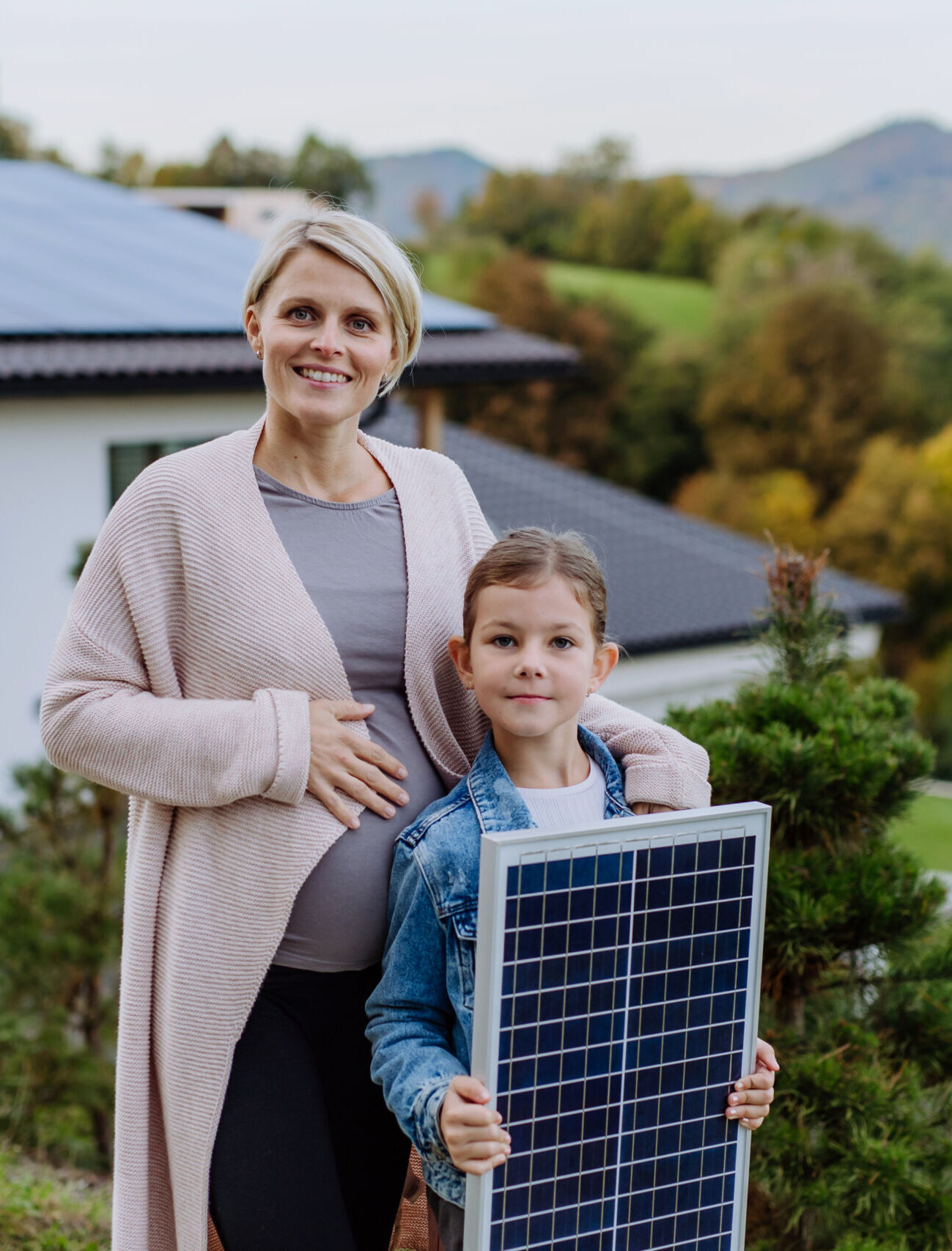Mother with her little daughter near their house with solar panels. Alternative energy, saving resources and sustainable lifestyle concept. Solar Energy Solutions